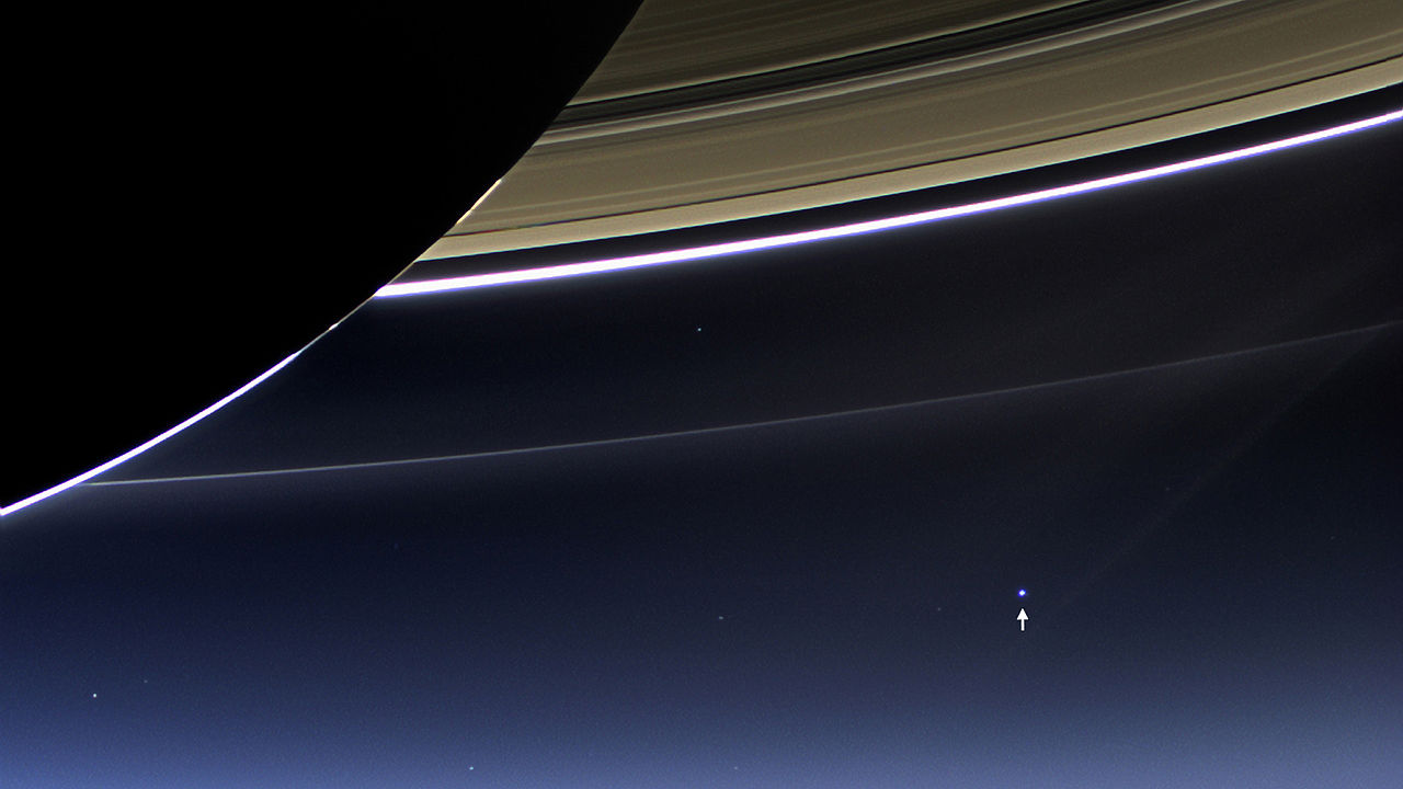 Großaufnahme von Saturn und eines Teils seiner Ringe. Im Hintergrund ist am schwarzen Himmel ein leuchtender Punkt mit einem weißen Pfeil markiert.