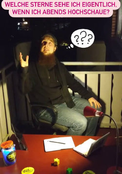 Michael Büker sitzt auf einem Bürostuhl auf einem Balkon, vor sich ein niedriger Tisch mit Sternen-Deko, Computern, Notizblock und einer Schreibtischlampe.